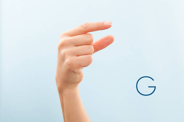 アメリカ手話言語。G 文字を示す女性の手は、青の背景に分離.  - 写真・画像