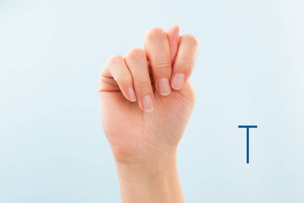 American sign language. Female hand showing letter T isolated on blue background.  - Photo, Image