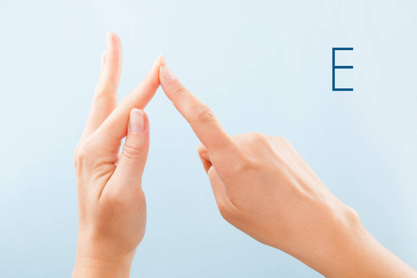 Алфавит с пальцами. Женщины руки изолированы на синем фоне, показывая глухонемой BSL алфавит буква Е
. - Фото, изображение