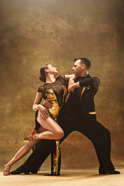 Dance ballroom couple in gold dress dancing on studio background. - 写真・画像