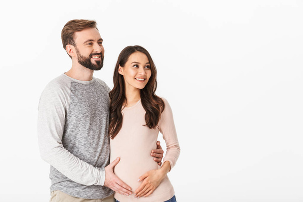 Photo of cheerful young man standing with his pregnant woman isolated over white background wall. Looking aside. - Foto, imagen