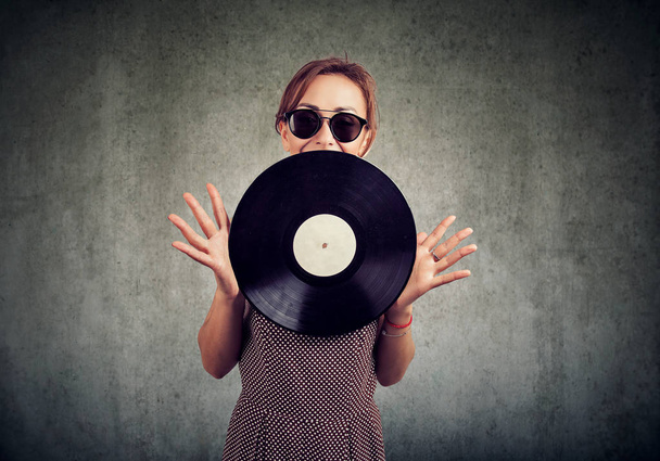 Joyful beautiful young woman in sunglasses showing a vintage vinyl - Photo, Image