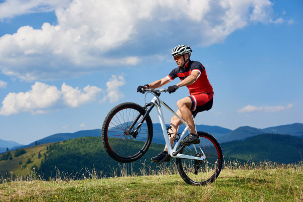 Nuori urheilija turisti biker ammatillinen urheiluvaatteet kääntämällä yhden pyörän pyörän vuoren mäellä kirkkaan sininen taivas tausta, Aktiivinen elämäntapa ja extreme sport käsite
  - Valokuva, kuva