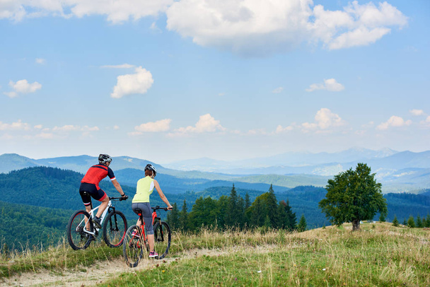プロフェッショナルなスポーツウェアと明るい日当たりの良い夏の日、アクティブなライフ スタイルと幸せな関係概念で山道にクロスカントリー サイクリング自転車にヘルメットで自転車カップル - 写真・画像
