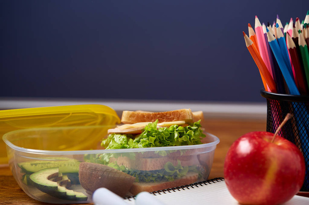 Concepto de descanso para el almuerzo escolar con lonchera saludable y útiles escolares en escritorio de madera, enfoque selectivo
. - Foto, Imagen