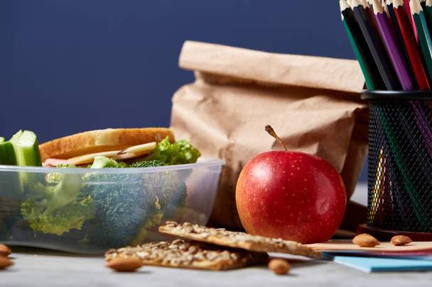 Back to School concept, school supplies, biscuits, packed lunch and lunchbox on white desk, selective focus, close-up. - Fotó, kép