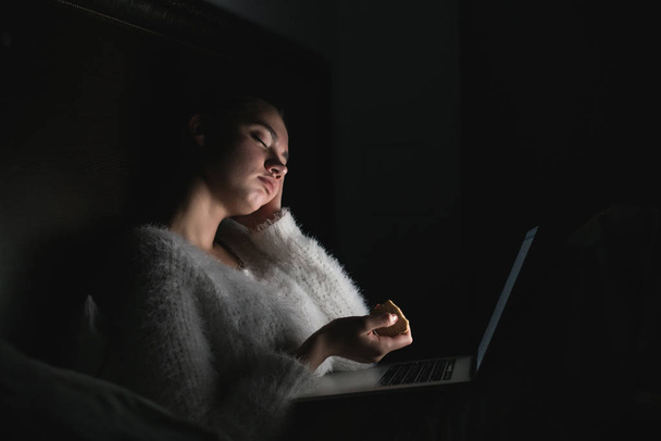 young girl sitting in bed late at night and watching a boring movie on her laptop, falling asleep - Foto, Bild
