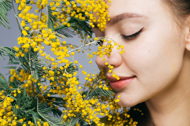 beautiful young girl enjoys a fragrant yellow mimosa, loves the spring - Фото, изображение