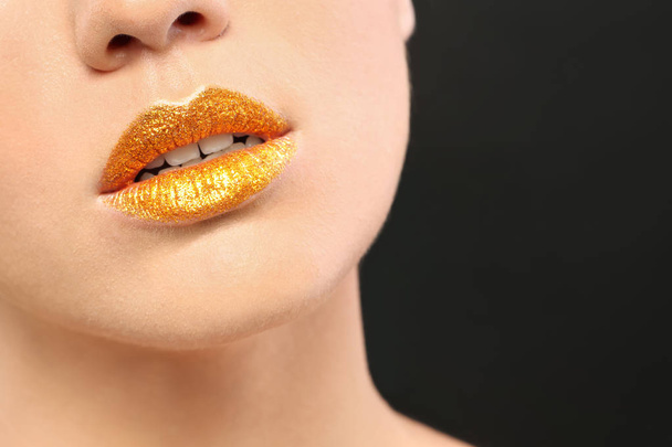 Beautiful young model with golden lips makeup on black background - Foto, Imagem