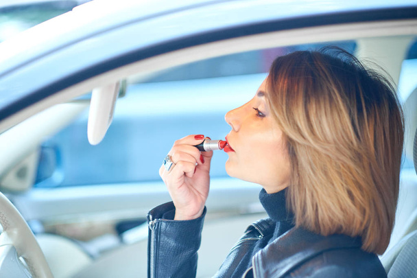 Menina bonita dirigindo um carro pinta lábios com batom vermelho
 - Foto, Imagem