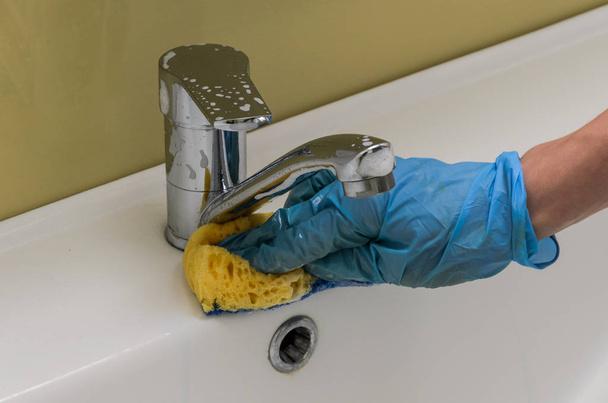 A woman in gloves washes the plumber and a tap with a rag in the bathroom with household chemicals - Valokuva, kuva