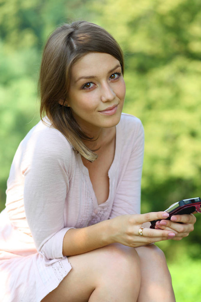 Young beautiful blonde woman reading a message on a cell phone, summer part outdoors - Foto, imagen