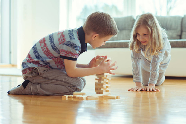 Two happy siblings playing a game with wooden blocks at home joyfully  - Foto, Imagem