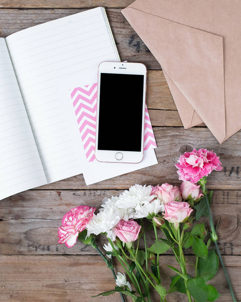 Phone with paper and beautiful flowers on wooden table - Foto, imagen