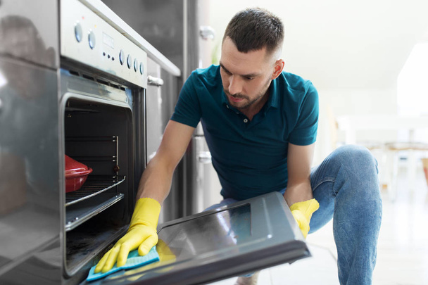 man with rag cleaning oven door at home kitchen - Fotografie, Obrázek