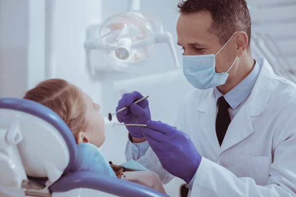 Experienced male dentist using dental tool - Фото, изображение