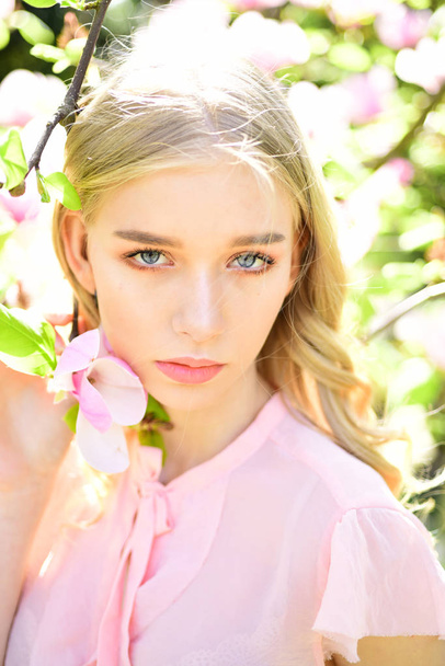 Charming blond woman relaxing and breathing fresh aroma of blooming magnolia outdoors in garden, sun glare effect. Spring time and unity with nature concept. - Photo, Image