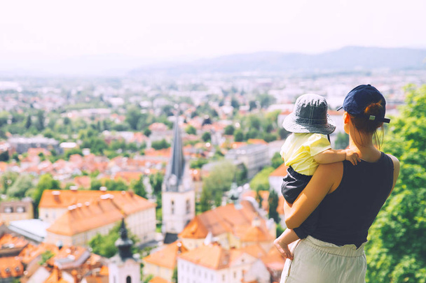 Woman and child on background of panoramic view with red roofs of Ljubljana City. Springtime or Summer in Slovenia. Family travel Europe. Happy smiling mother with little daughter outdoors - Photo, image