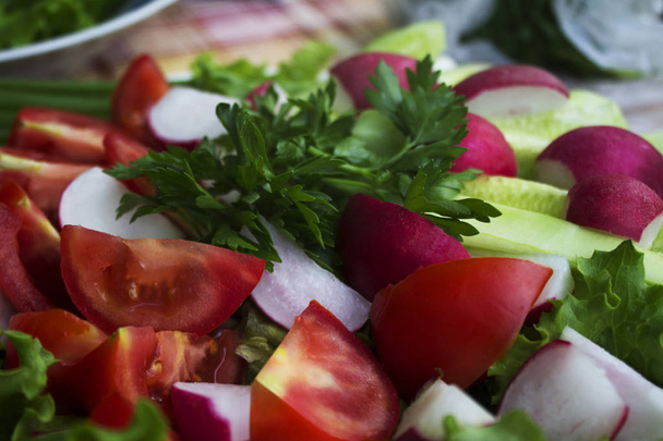 Tuoreiden vihannesten viipalointi: tomaatit, kurkut, retiisi, salaatti ja persilja, lähikuva
. - Valokuva, kuva