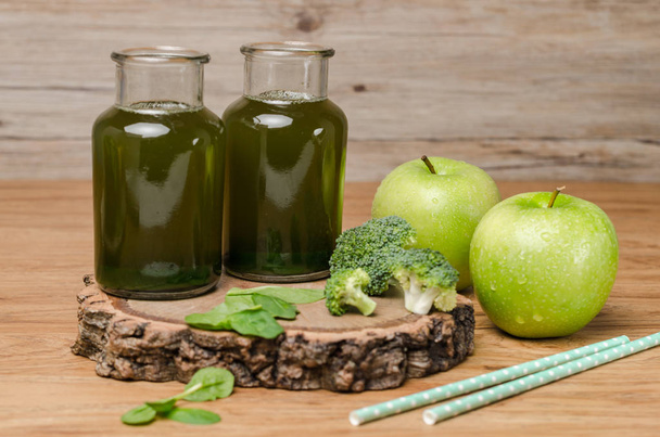 Green fresh leafy greens smoothie in glass jar, spinach leaves, apple, broccoli and lemon. Refreshing healthy drink on wooden table background - Foto, immagini