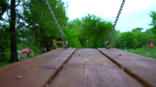 Balanço de madeira em correntes de aço balançando em um parque de crianças vazio
 - Filmagem, Vídeo