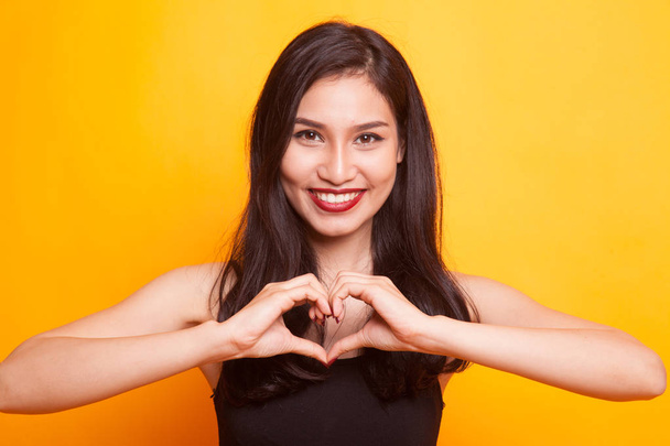Young Asian woman gesturing heart hand sign on yellow background - Foto, Bild