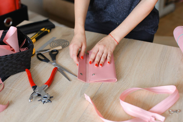 Γυναικείο πρόσωπο κάνοντας ροζ δερμάτινο πορτοφόλι με εργαλεία στο ατελιέ. - Φωτογραφία, εικόνα