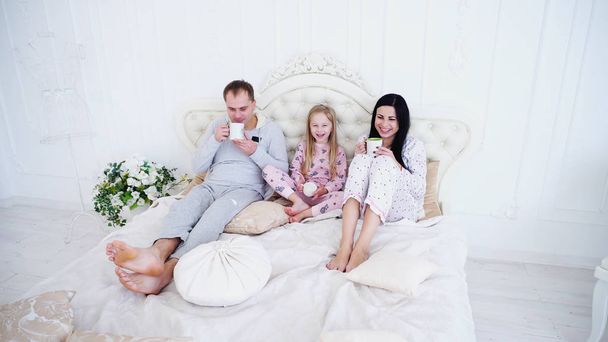 Szczęśliwych rodziców z córeczką, leżąc w łóżku i picie herbaty w sypialni. - Zdjęcie, obraz