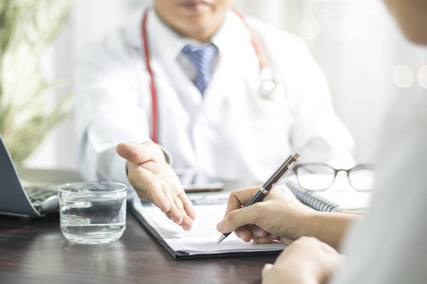 Доктор вводить підписання пацієнта на медичні записи перед лікуванням хвороби на столі в лікарні
  - Фото, зображення