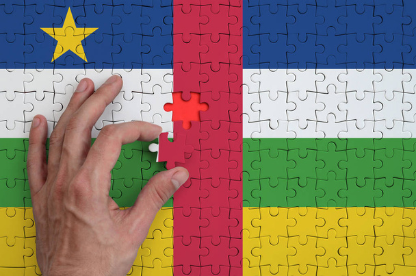 Bandera de la República Centroafricana se representa en un rompecabezas, que la mano del hombre completa para doblar
. - Foto, Imagen