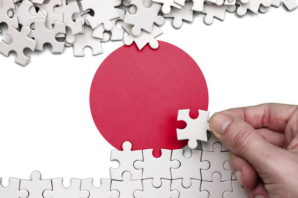 Флаг Японии изображен на столе, на котором человеческая рука складывает пазл белого цвета
. - Фото, изображение
