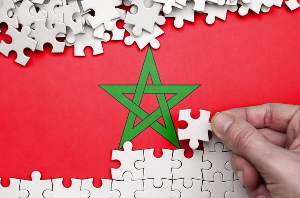 Bandera de Marruecos se representa en una mesa en la que la mano humana pliega un rompecabezas de color blanco
. - Foto, Imagen