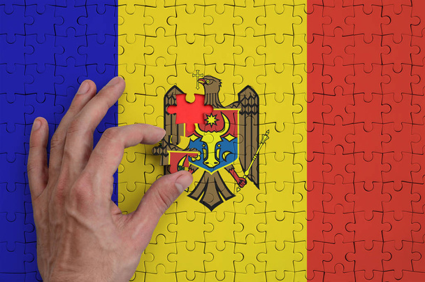 Σημαία της Μολδαβίας απεικονίζεται σε ένα παζλ, το οποίο ολοκληρώνει το χέρι του άνδρα να πάει πάσο. - Φωτογραφία, εικόνα