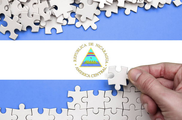 Bandera de Nicaragua se representa en una mesa en la que la mano humana dobla un rompecabezas de color blanco
. - Foto, Imagen
