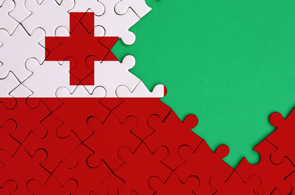 Die Tonga-Flagge ist auf einem abgeschlossenen Puzzle mit freiem grünen Kopierraum auf der rechten Seite abgebildet.. - Foto, Bild