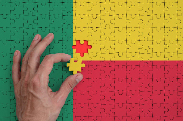 Флаг Бенина изображен на головоломке, которую рука человека завершает сложить
. - Фото, изображение