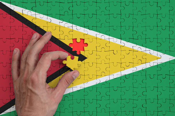 Guyanan lippu on kuvattu palapelissä, jonka miehen käsi täydentää taittamaan
. - Valokuva, kuva