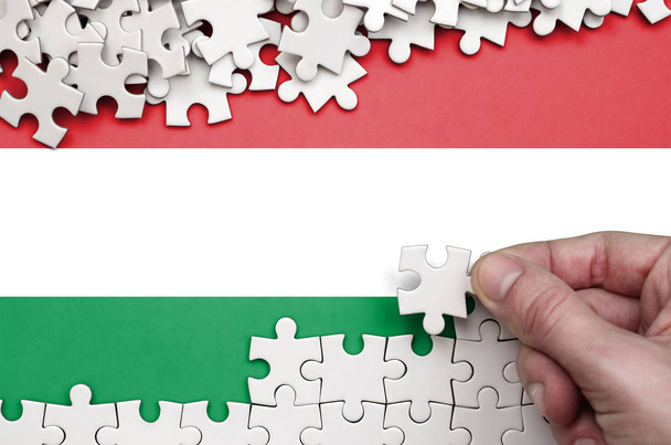 Vlag van Hongarije is afgebeeld op een tafel waarop de menselijke hand plooien een puzzel van witte kleur. - Foto, afbeelding