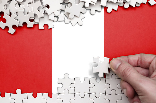 Peru flag  is depicted on a table on which the human hand folds a puzzle of white color. - Foto, Imagen