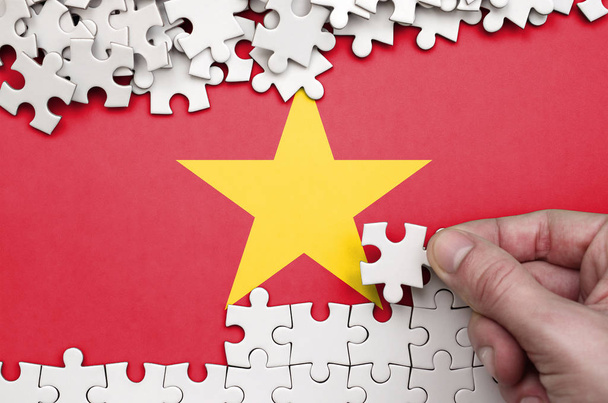 Die vietnamesische Flagge ist auf einem Tisch abgebildet, auf dem die menschliche Hand ein Puzzle weißer Farbe faltet.. - Foto, Bild