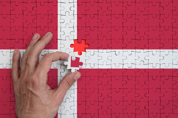 Vlag van Denemarken wordt afgebeeld op een puzzel, die de man hand voltooit te vouwen. - Foto, afbeelding