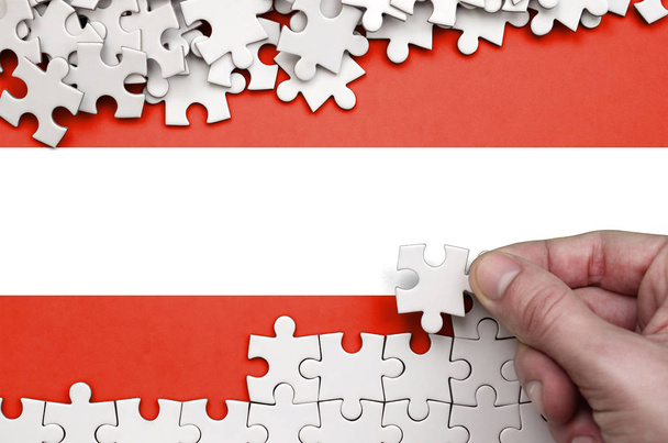 Bandera de Austria se representa en una mesa en la que la mano humana pliega un rompecabezas de color blanco
. - Foto, Imagen