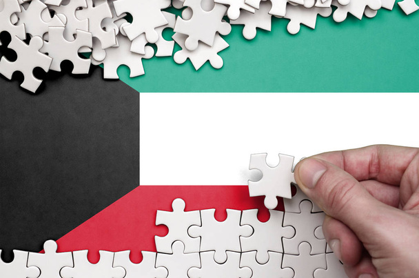 Bandera de Kuwait se representa en una mesa en la que la mano humana pliega un rompecabezas de color blanco
. - Foto, Imagen