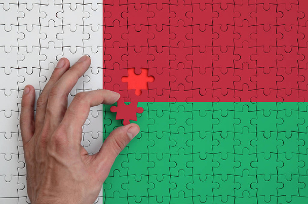Madagaskar-Fahne ist auf einem Puzzle abgebildet, das die Hand des Mannes zum Falten ausfüllt. - Foto, Bild