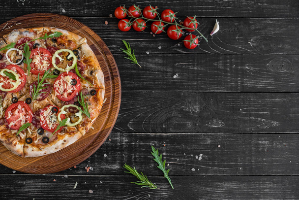 Vegetables, mushrooms and tomatoes pizza on a black wooden background. It can be used as a background - Photo, Image