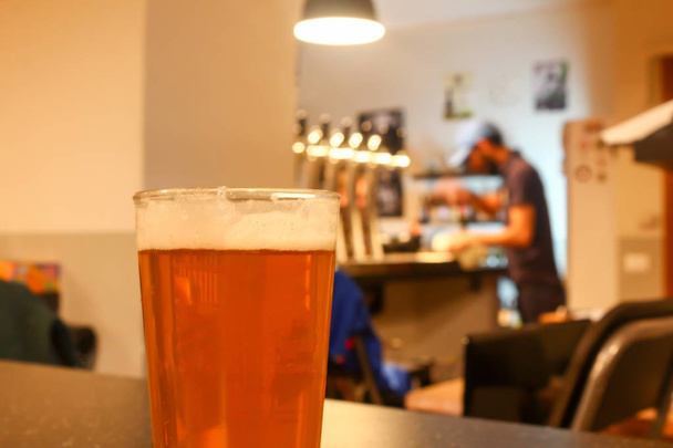 Lasi kevyt appelsiini mehukas veneet olutta veneet baari pubissa taustalla kiiltävä olut hanat ja nuori mies parrakas baarimikko
  - Valokuva, kuva