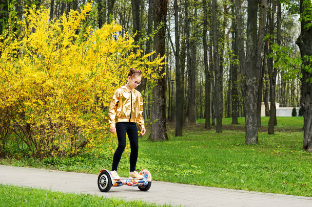active girl in a gold jacket rides balances on self balancing scooter - Foto, afbeelding
