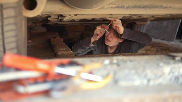 Mechanik mężczyzna pod samochód naprawia swój samochód w garażu - Materiał filmowy, wideo