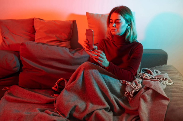 Портрет молодої леді ситіг з плоскою і використовуючи мобільний телефон на дивані, проводячи час вдома
 - Фото, зображення