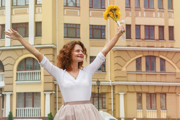 Uma menina feliz caminha pela cidade com um buquê de flores amarelas Gerber
 - Foto, Imagem